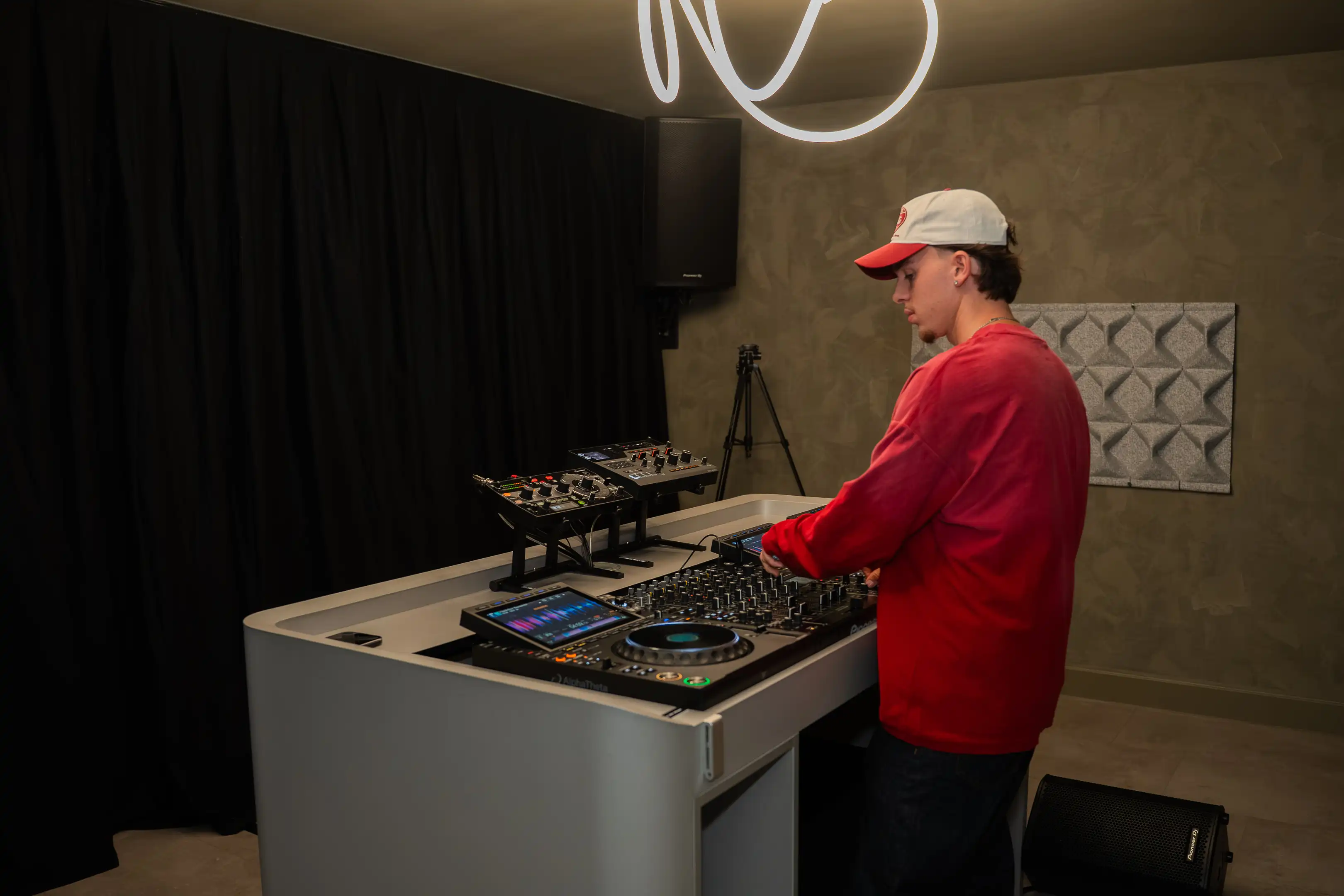 Een DJ met pet draait achter de booth, onder de neonlijn aan het plafond
